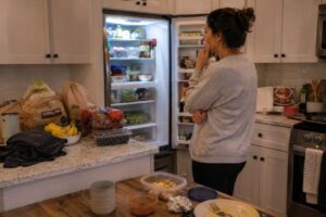 Parent overwhelmed while looking into cluttered fridge filled with groceries and leftovers