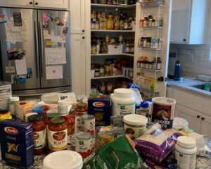 Overwhelmed parent unpacking duplicate groceries into a cluttered kitchen