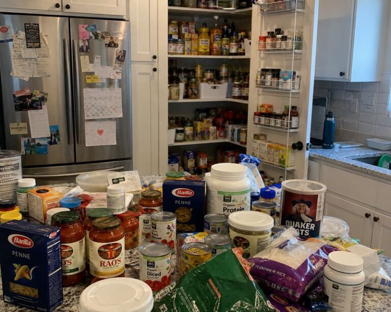 Overwhelmed parent unpacking duplicate groceries into a cluttered kitchen